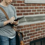 standing man in gray crew-neck long-sleeved shirt leaning on brown bricked wall